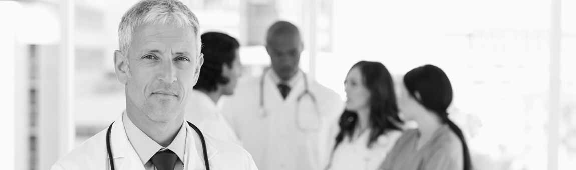 Klinikarzt, im Hintergrund ist Klinikpersonal zu sehen.